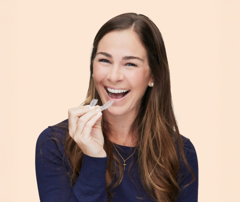 smiling patient inserting invisalign clear aligners