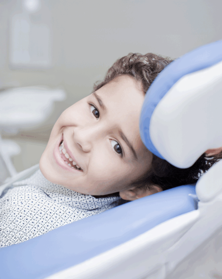 A young boy sitting in a blue dental chair and smiling, ready to receive pediatric dentistry.