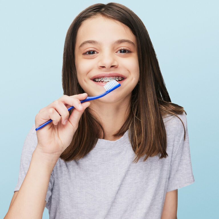 smiling girl wearing braces brushing her teeth