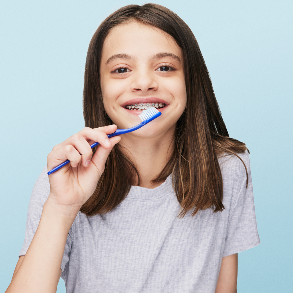 smiling girl wearing braces brushing her teeth