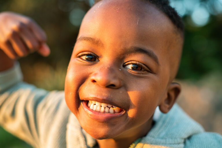 Close-up portrait of a cute little African-American boy laughing while playing outside on a sunny afternoon