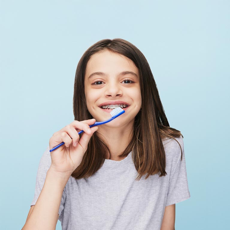 smiling girl wearing braces brushing her teeth 1
