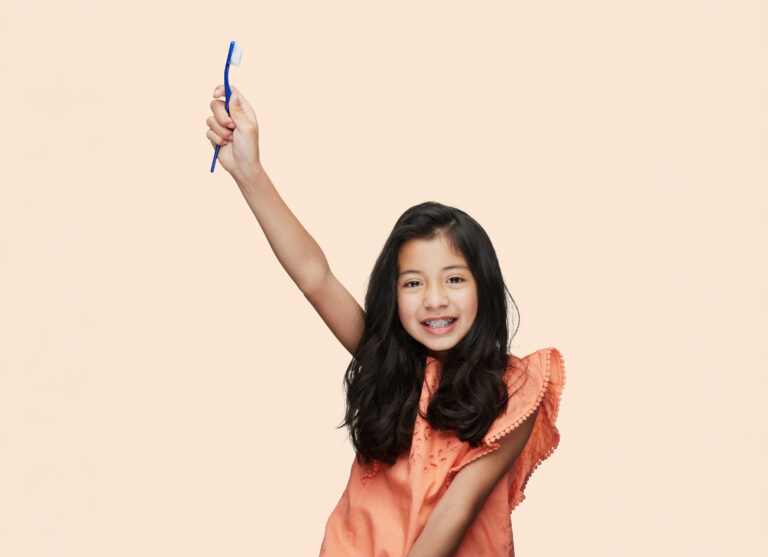 A Young Patient At Maccaro Orthodontics Holding Up A Toothbrush Looking Proud